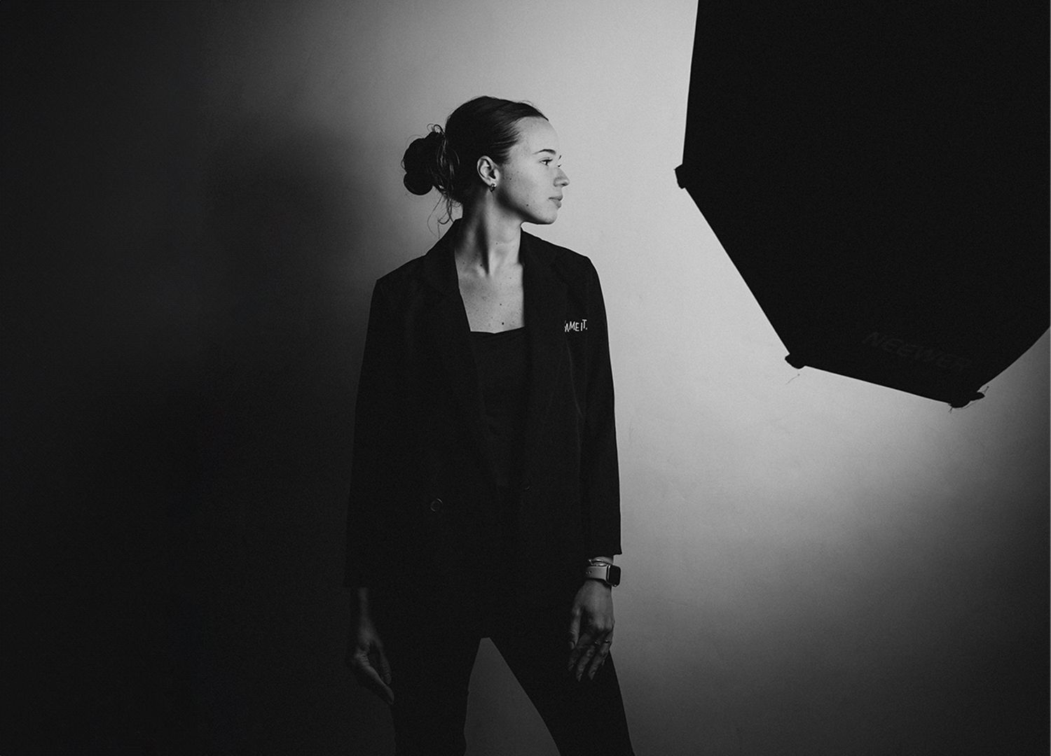 Stylish black and white studio portrait with figure in blazer looking toward an octagonal light modifier.