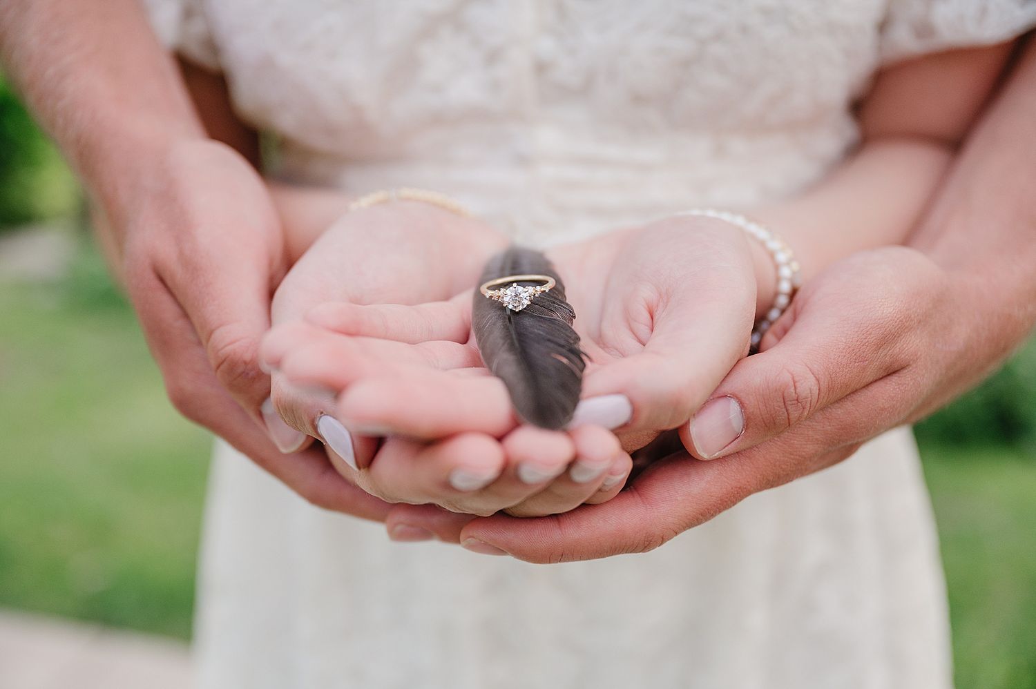 Cupped hands in white lace dress gently hold a tiny gray baby bird in an outdoor garden setting.