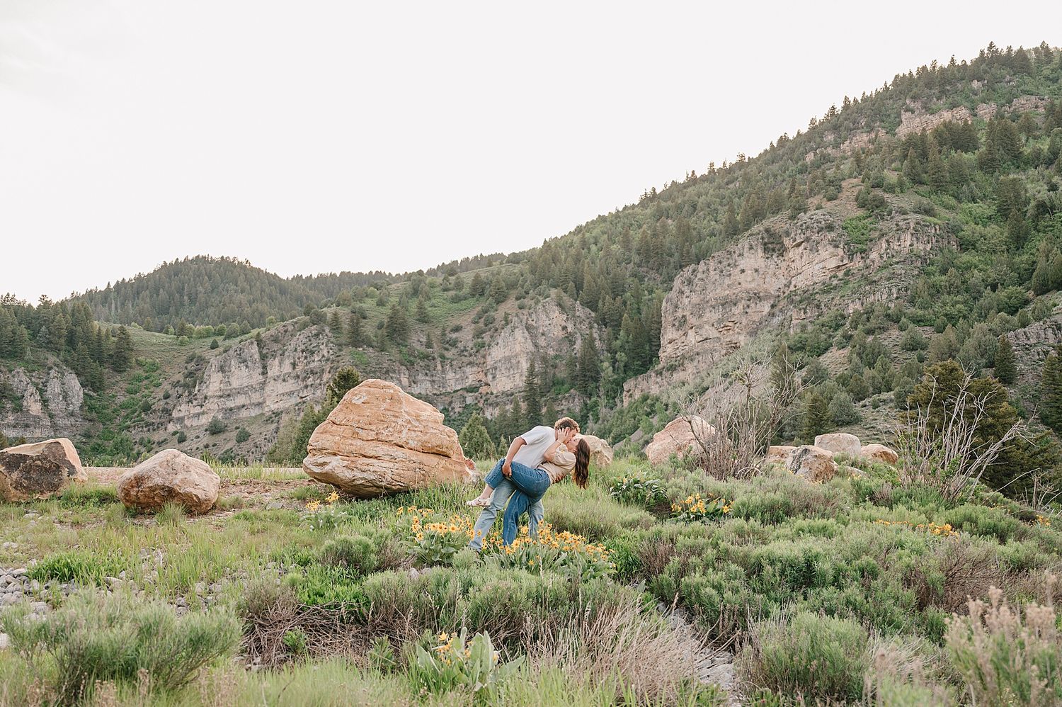 A couple dressed in outdoor attire share a moment together while hiking along a scenic mountainous trail at sunset.
