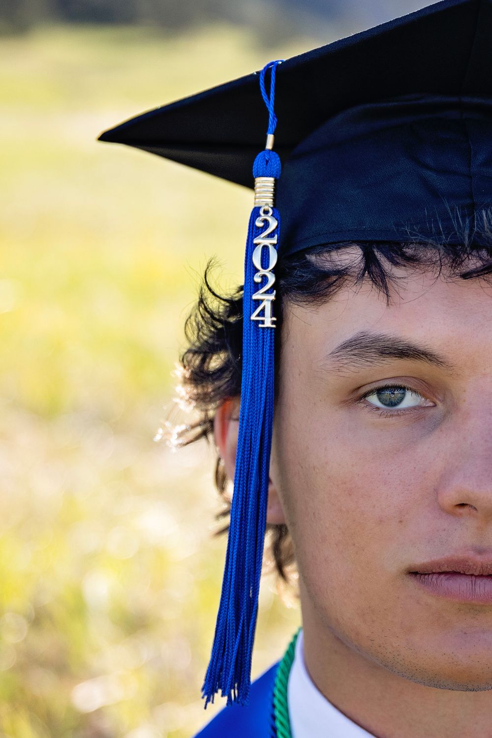 A graduation cap with a blue 2024 tassel is shown against a blurred outdoor background.