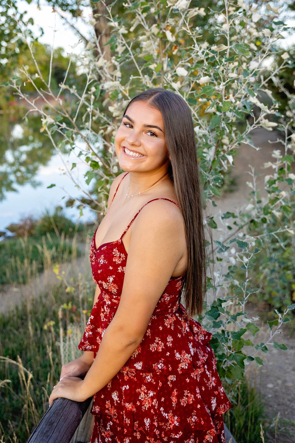 A bright summer portrait in a floral red dress against a backdrop of silver birch trees and natural foliage.