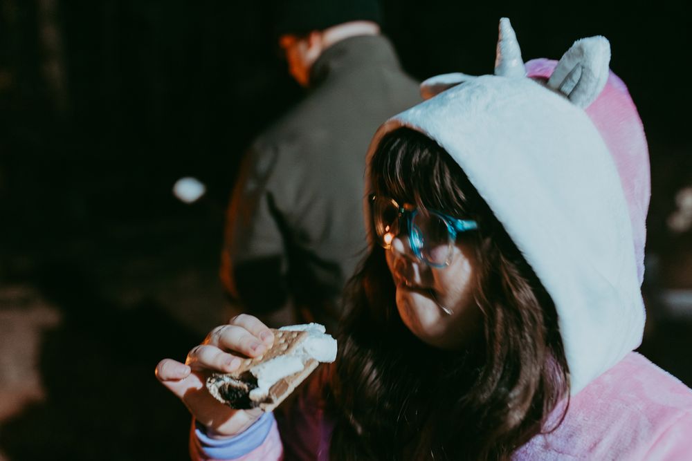 Little girl in unicorn onesie eating a smore. Night time photo, Whitney Popp photographer.