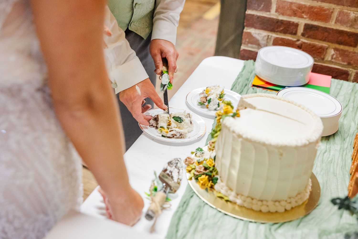 Couple cutting into a white two-tier wedding cake adorned with flowers on a rustic table setting.