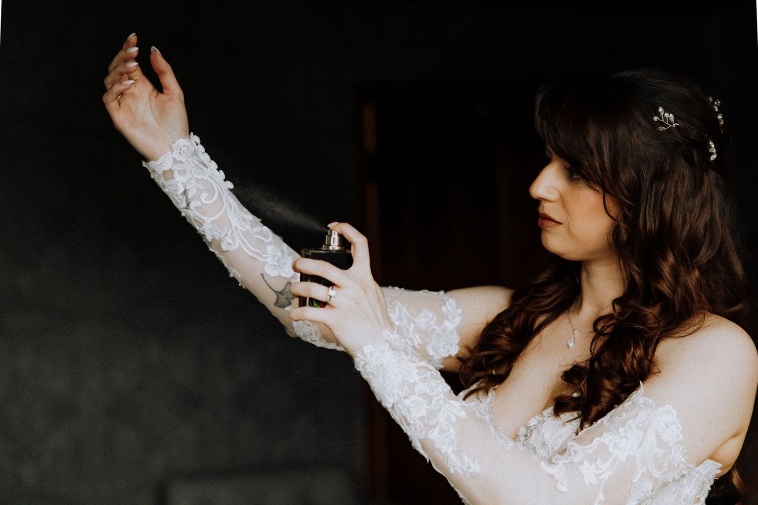 A bride in a long-sleeve lace wedding dress reaches out gracefully against a dark background.