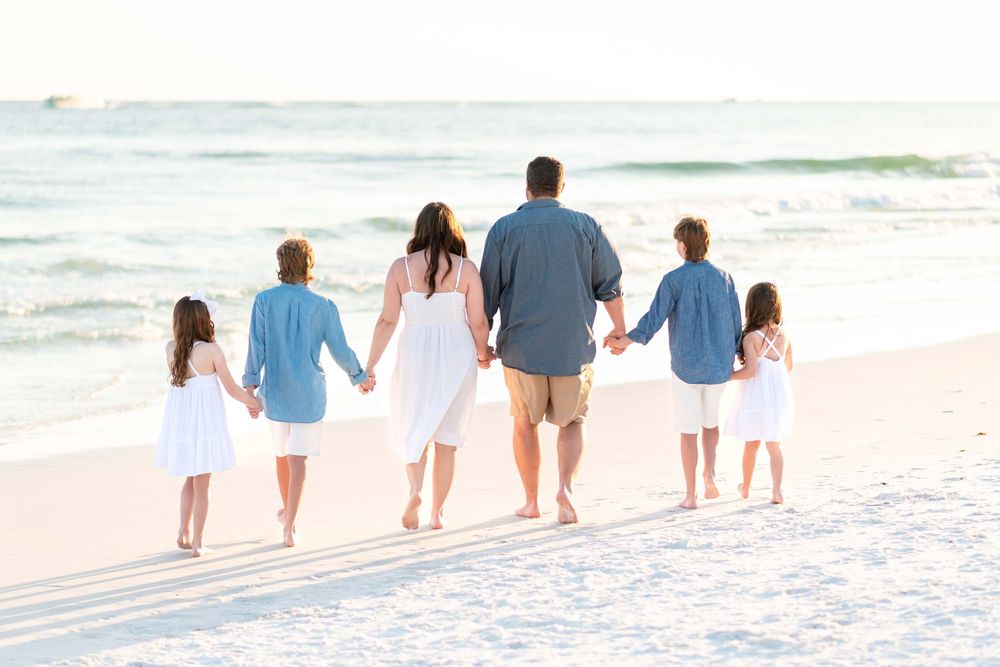 Family of six walking together along the beach shore during sunset while wearing coordinated blue and white outfits.