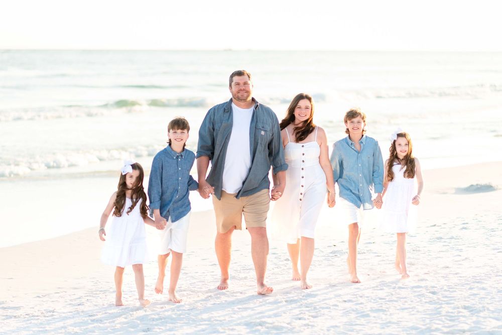 A family of five dressed in blue and white walking together on a sunny beach.