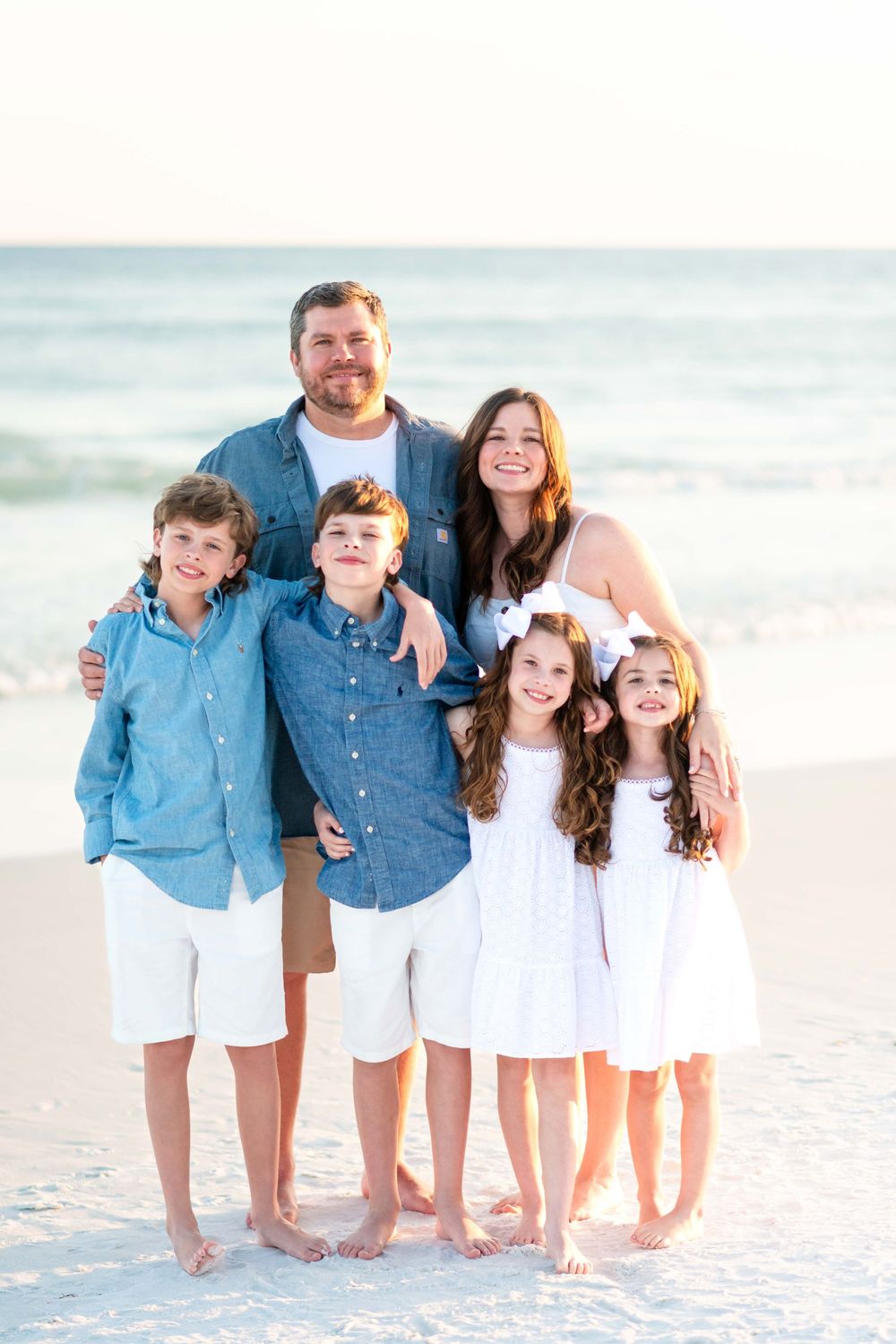 A happy family wearing coordinated blue and white outfits poses together on a sunny beach.