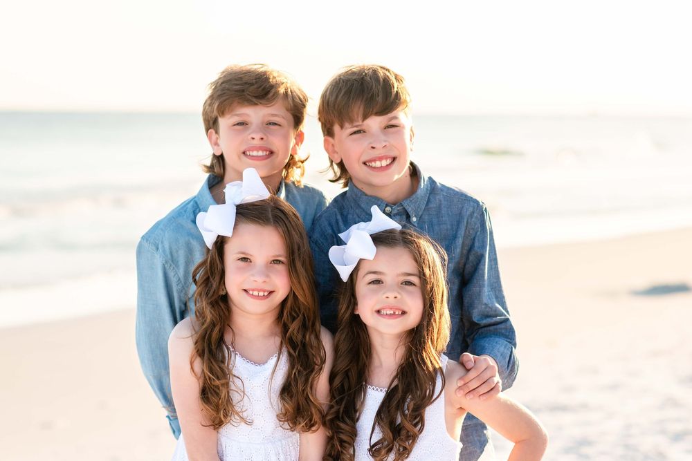 Happy siblings pose together for a casual portrait at the beach on a bright sunny day.