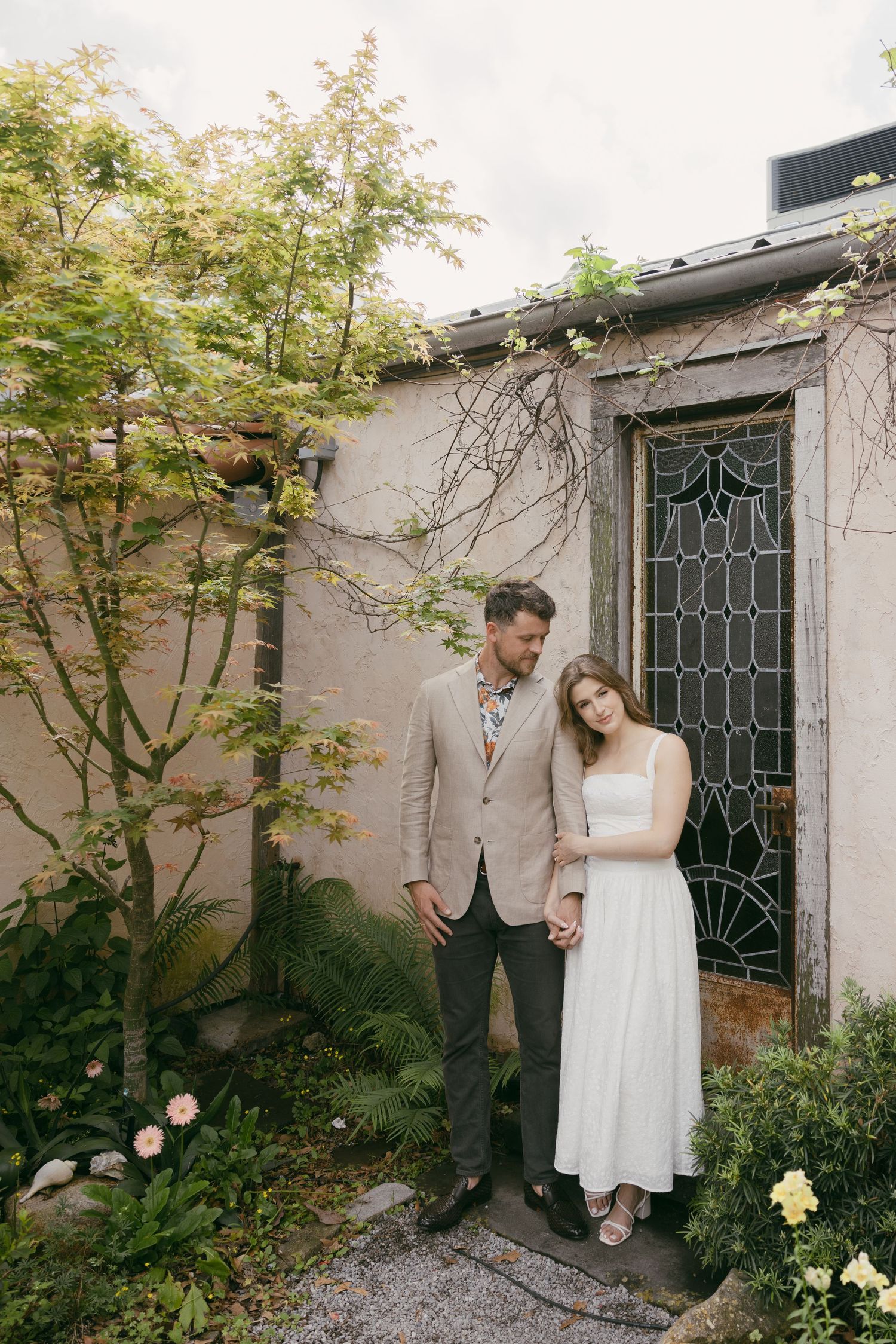 Couple in vintage style clothing standing in elegant Victorian parlor room with wooden floors and flowing curtains.