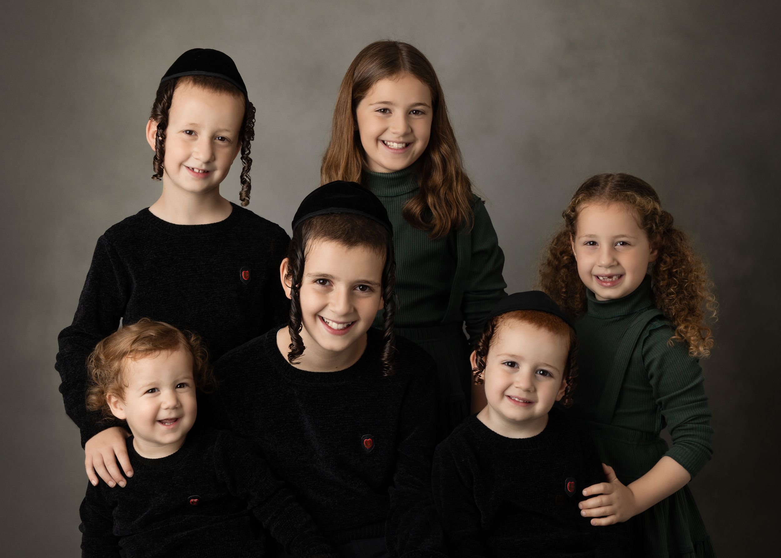 A family group wearing coordinated black outfits poses together in a professional studio setting.