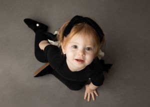 Baby in black outfit lying on grey floor looking up at camera.