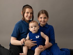Studio family portrait with three people wearing blue and black outfits against a grey backdrop.