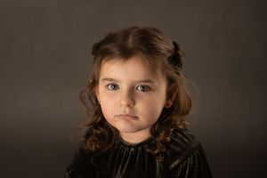 Studio portrait against dark background with dramatic lighting and curly brown hair.
