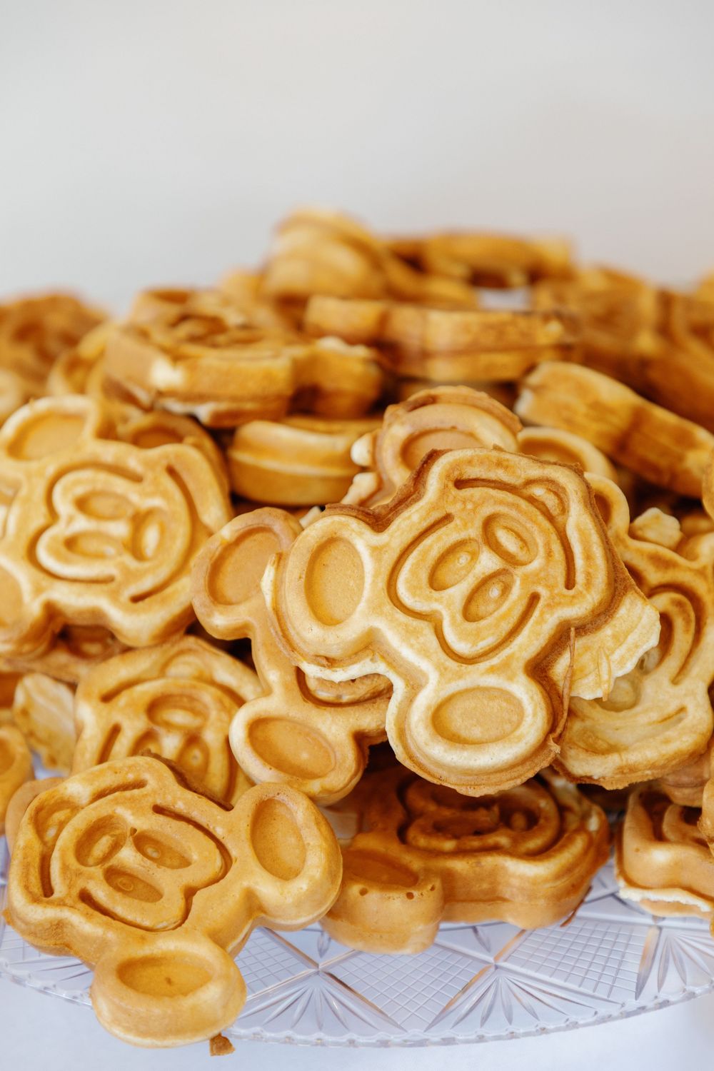 Stack of golden Mickey Mouse shaped waffles piled high on a crystal plate at a Disney themed birthday party.