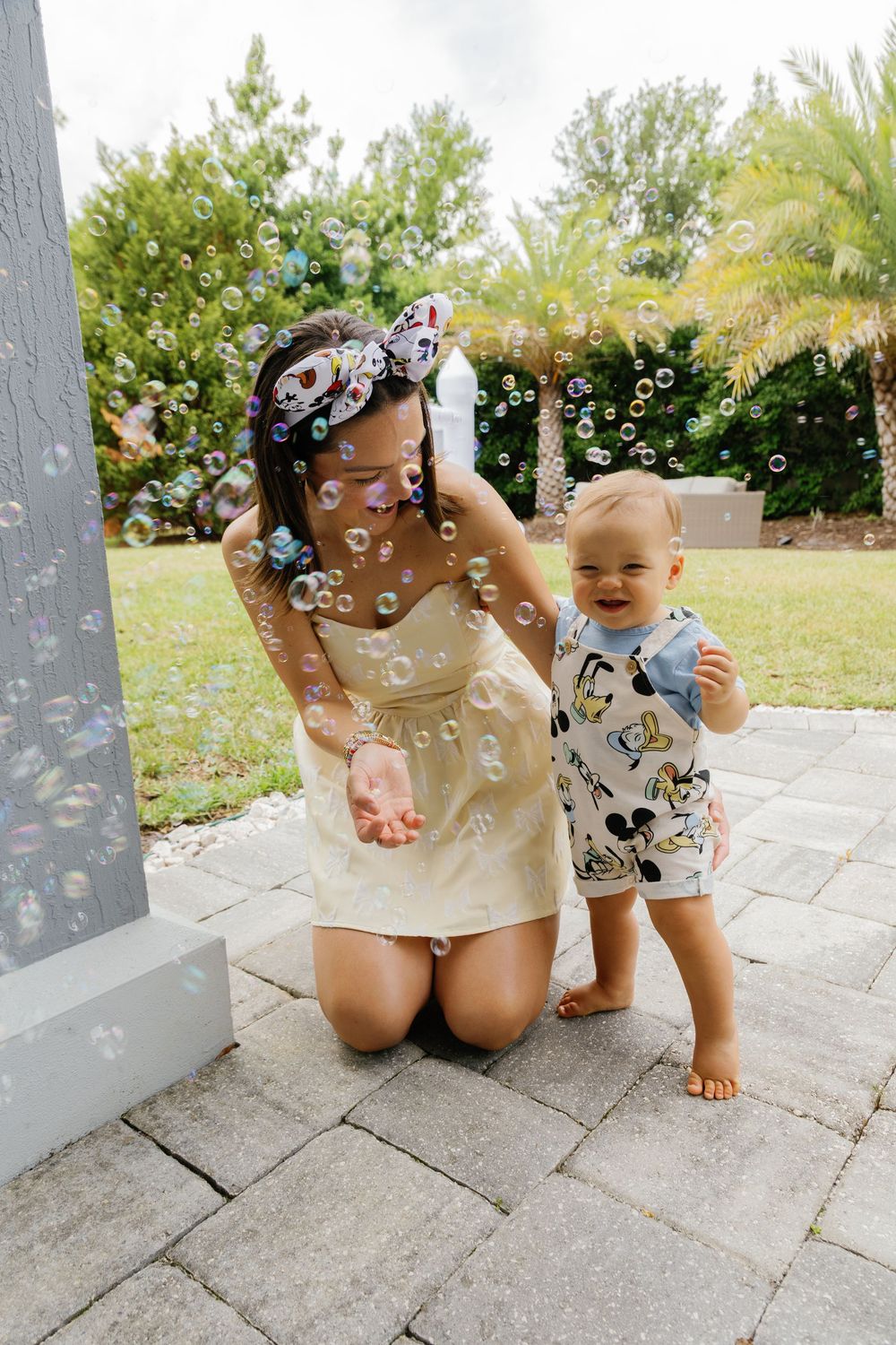 Mother kneeling with toddler playing with bubbles outdoors on patio.