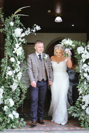 White floral archway decorates doorway entrance at elegant wedding venue with indoor lighting.