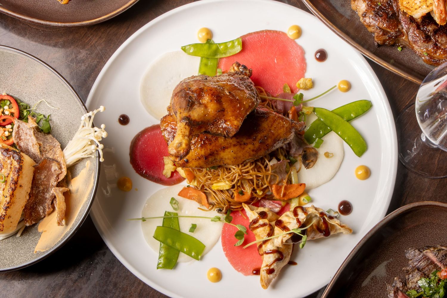 Elegant plated dish with roasted meat, vibrant red sauce, green garnishes and nuts on a white ceramic plate.