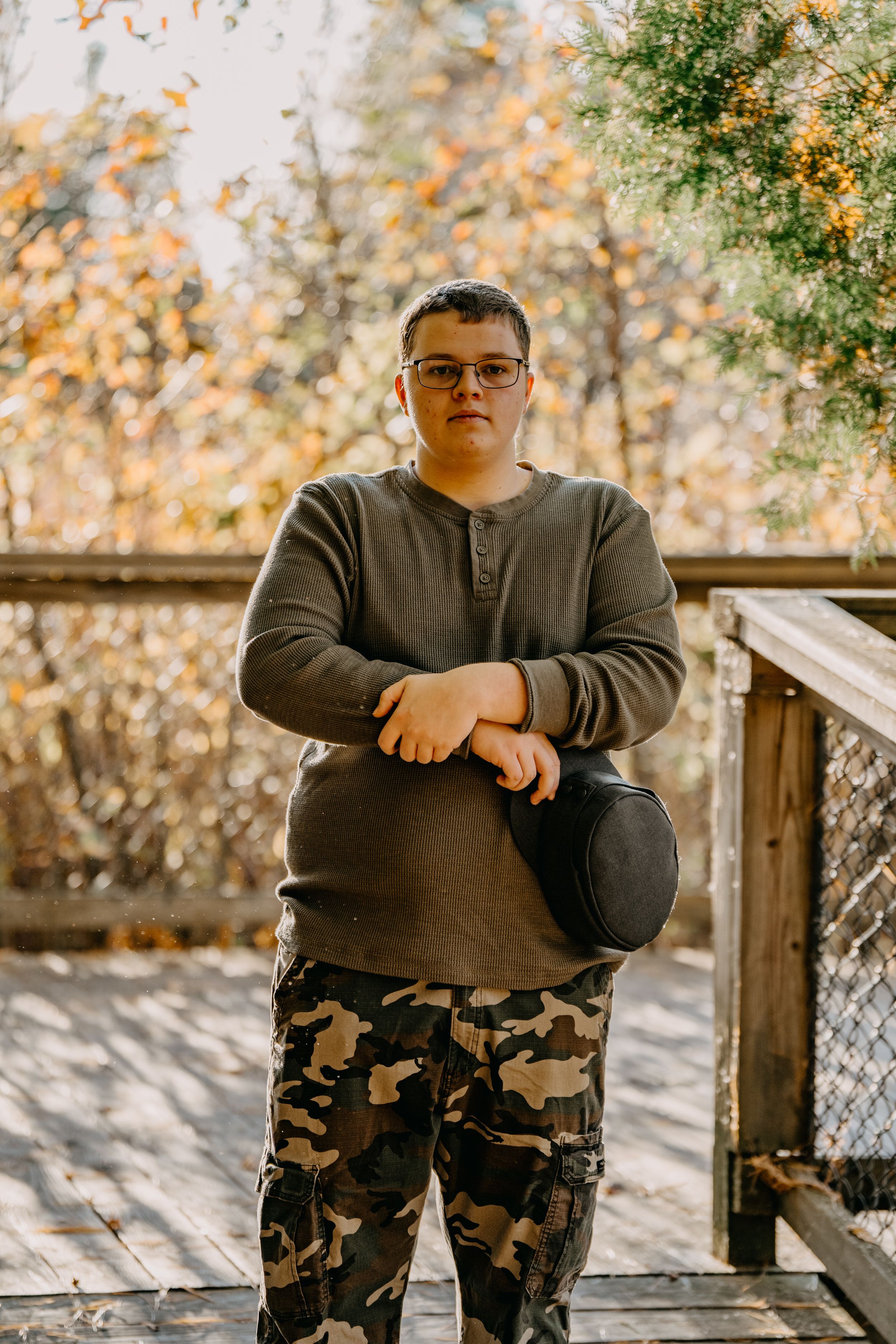 Person wearing brown sweater and camouflage pants poses on wooden deck during autumn season.