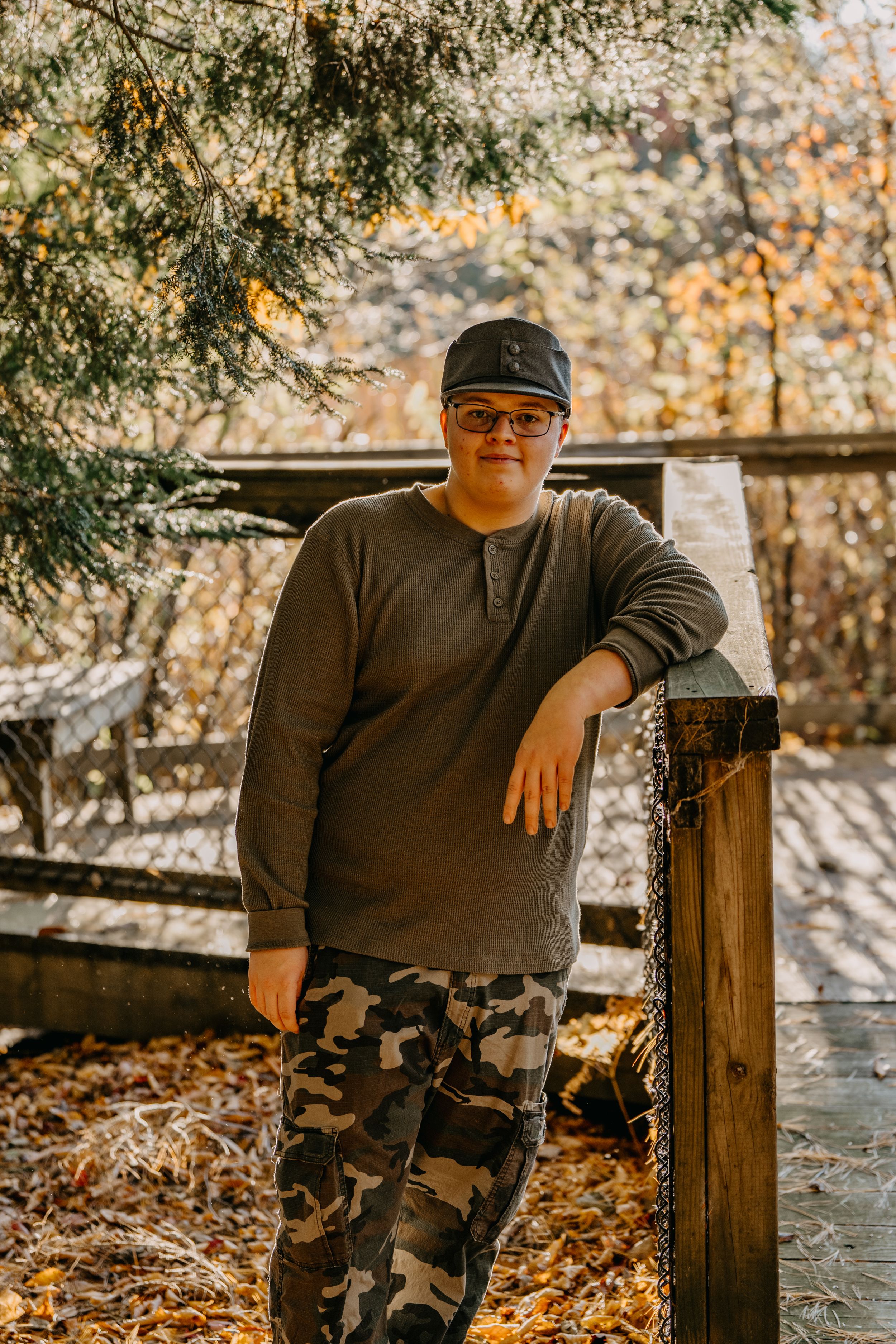 Autumn outdoor portrait session shows a subject seated on wooden fence posts surrounded by vibrant fall foliage.