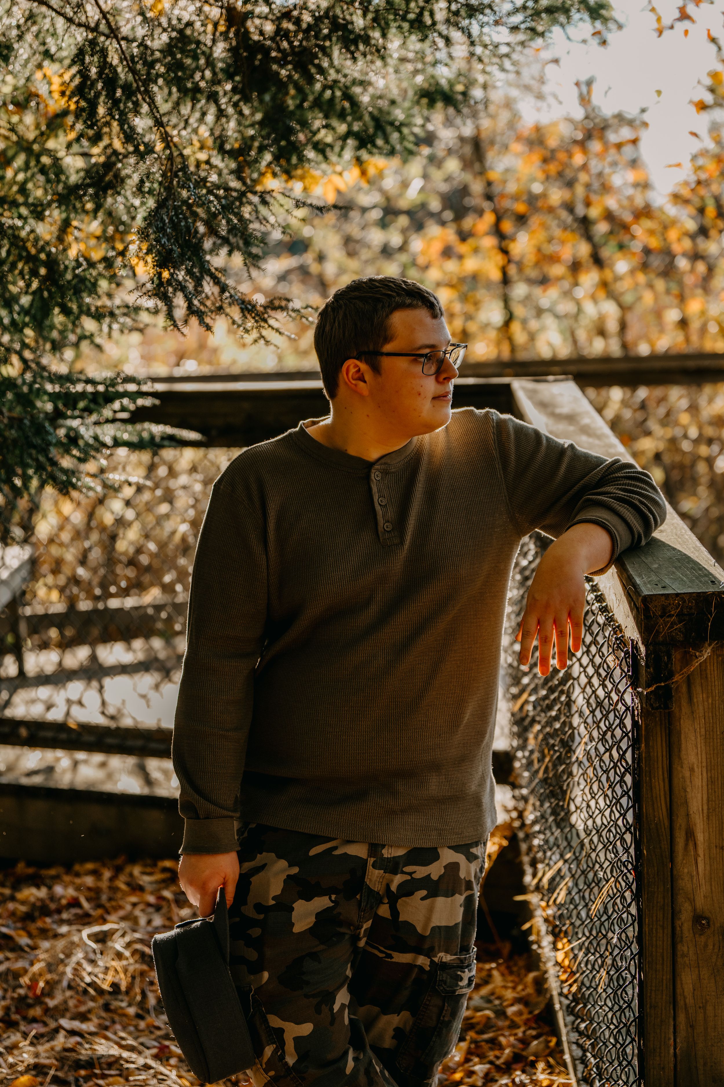 Person in casual wear leaning against wooden fence during autumn with blurred golden foliage background.