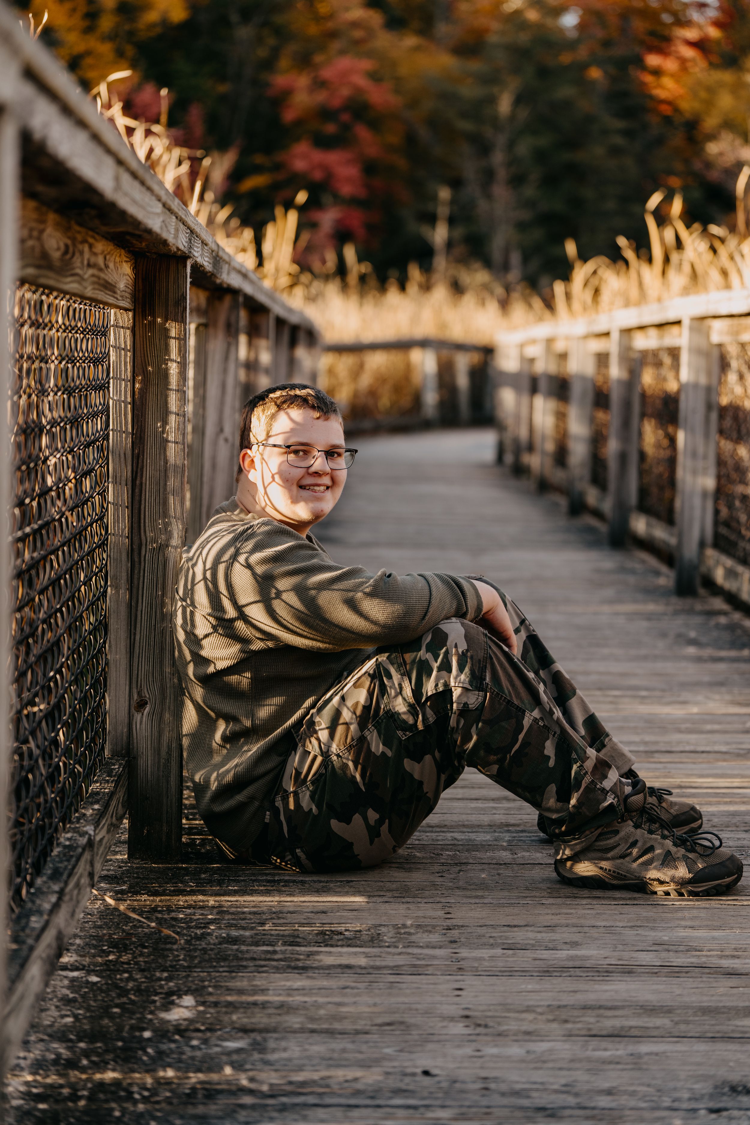A person sits on a wooden boardwalk surrounded by autumn foliage and golden light.