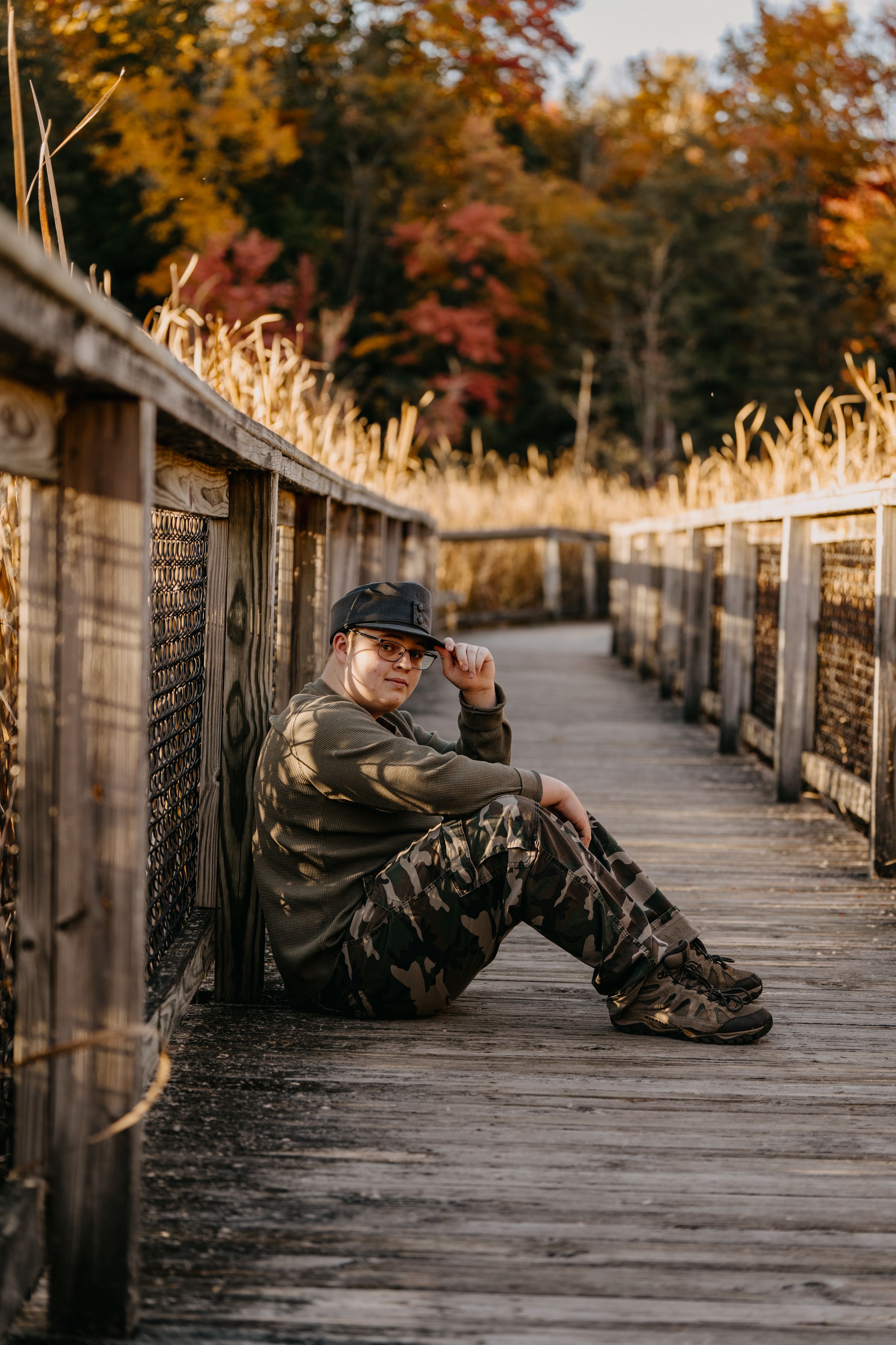 An autumn boardwalk with golden dry grass and fall foliage visible along a wooden walkway at sunset.