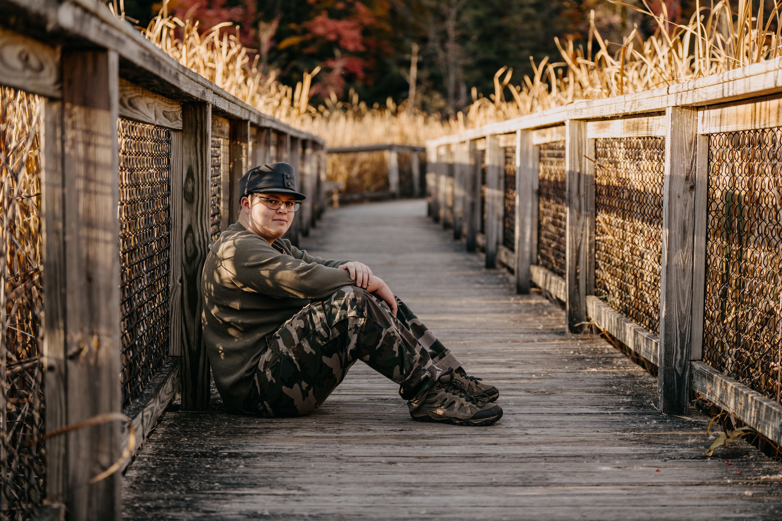 A solitary figure sits on a wooden boardwalk surrounded by tall dried grasses during golden hour.
