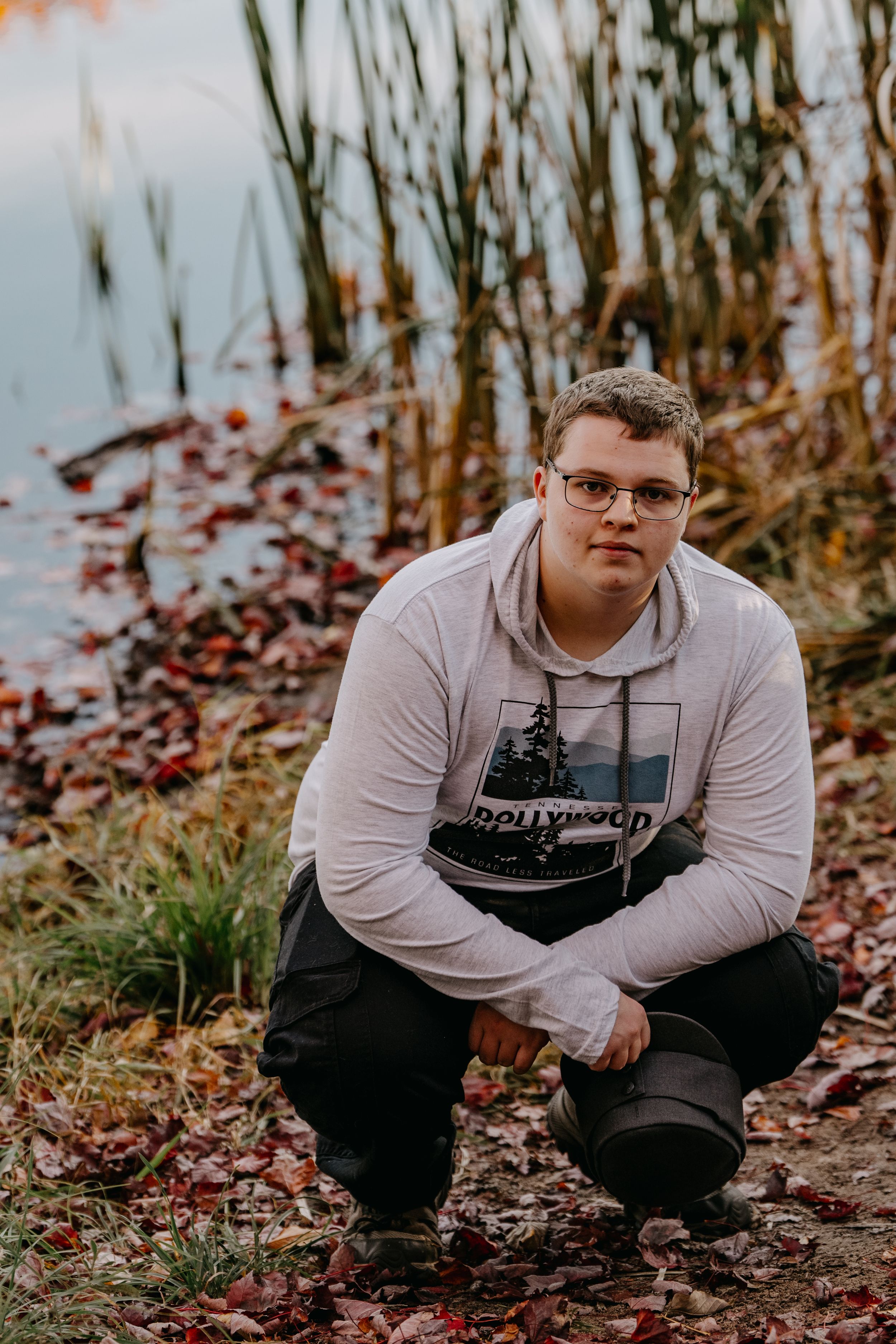 A casual portrait by a lake with cattails and fall foliage in the background.