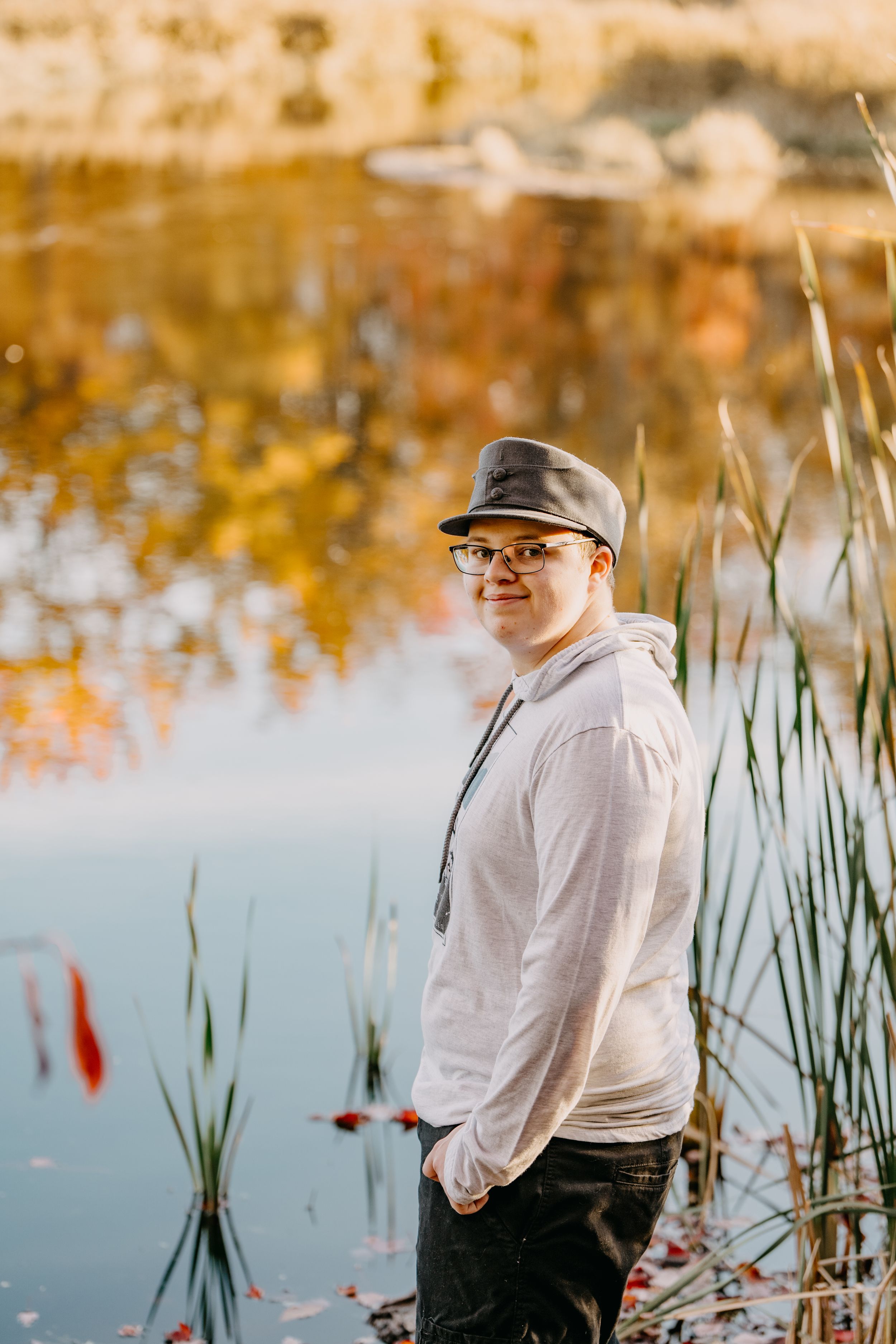Person stands beside tranquil pond wearing casual attire with autumn reflections in water.