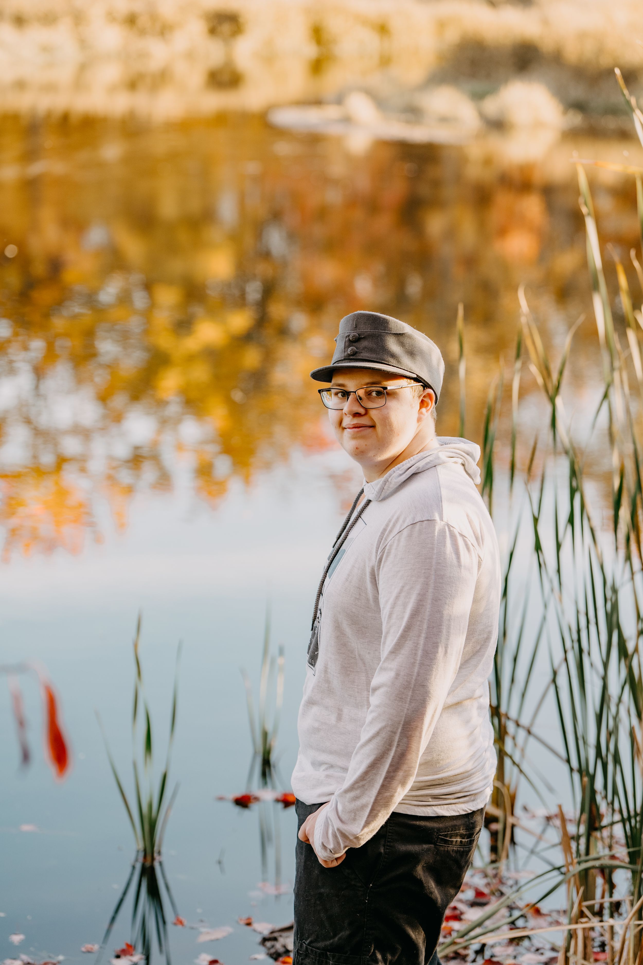 Person in white shirt and cap sits by tranquil pond with autumn reflections and cattails.