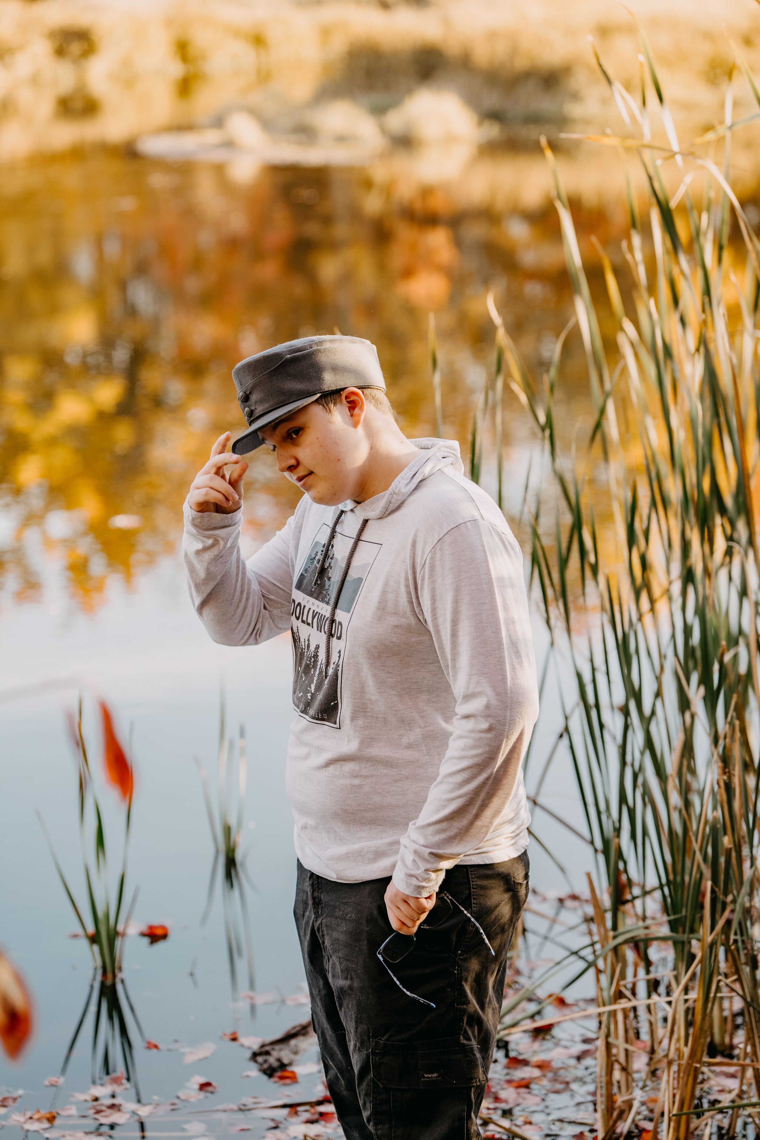 A casual portrait by water with golden reflections and cattails in late afternoon light.
