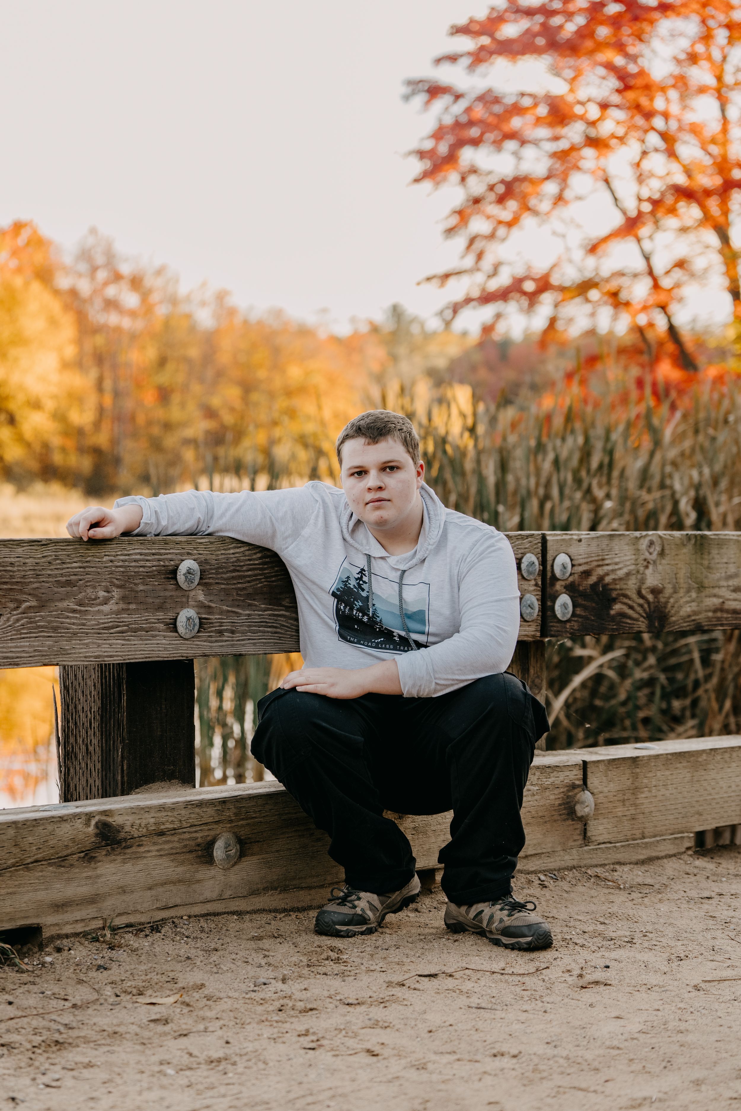 Person sits on wooden railing at sunset with autumn foliage glowing orange and yellow in background.