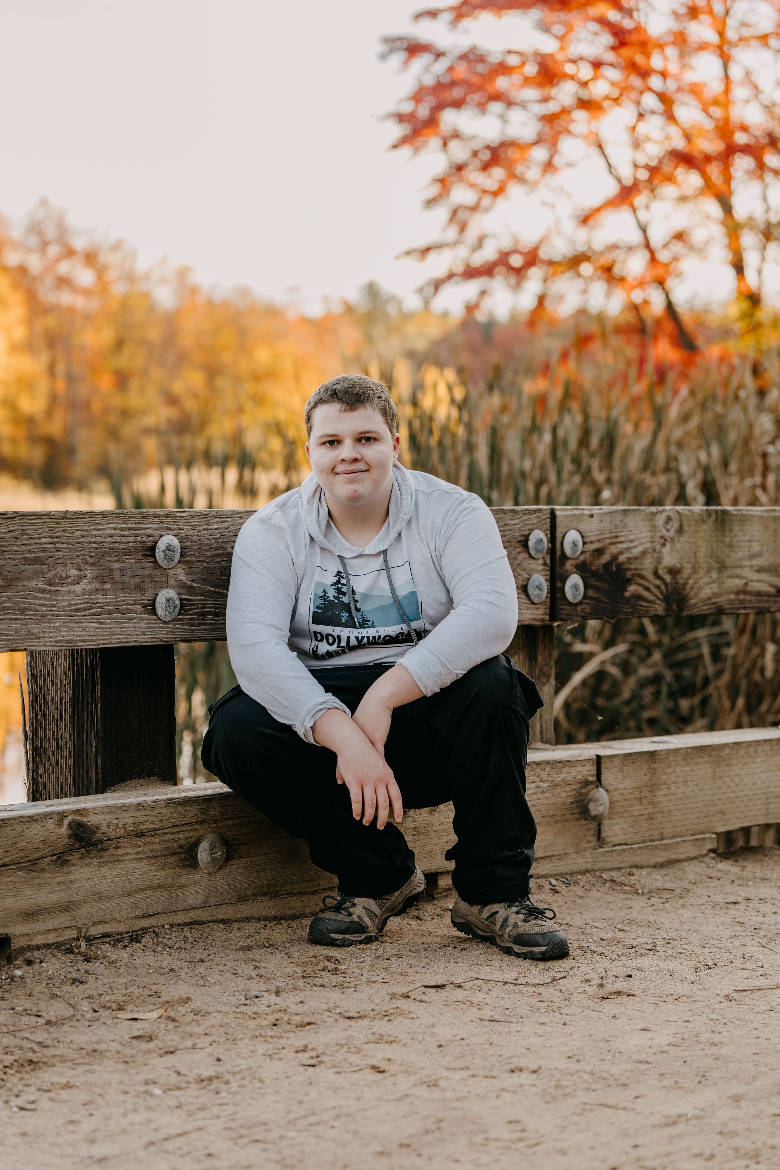 Someone sits on a wooden bench during autumn with orange trees in background.