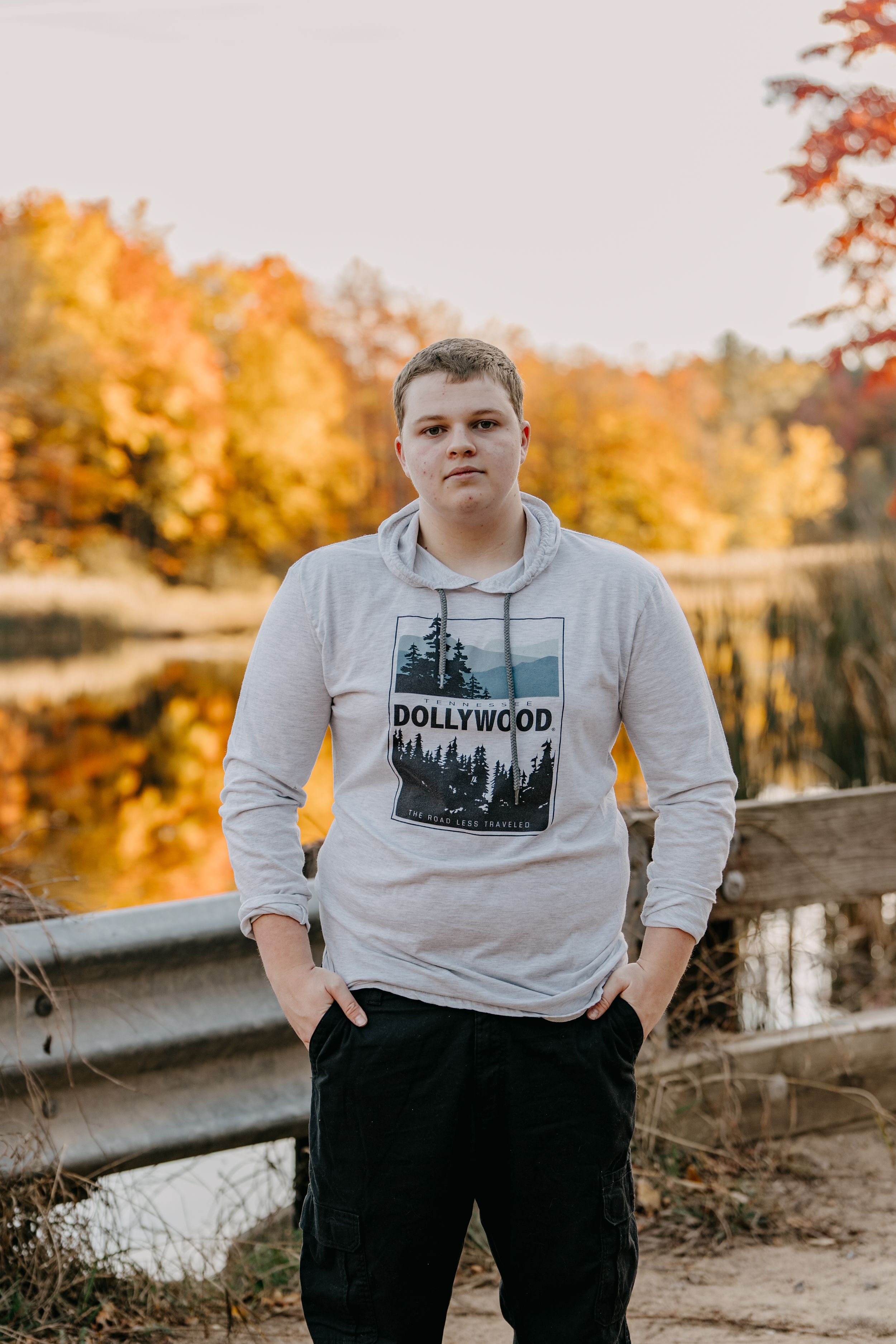 A casual portrait on a bridge with autumn foliage and golden light in background.