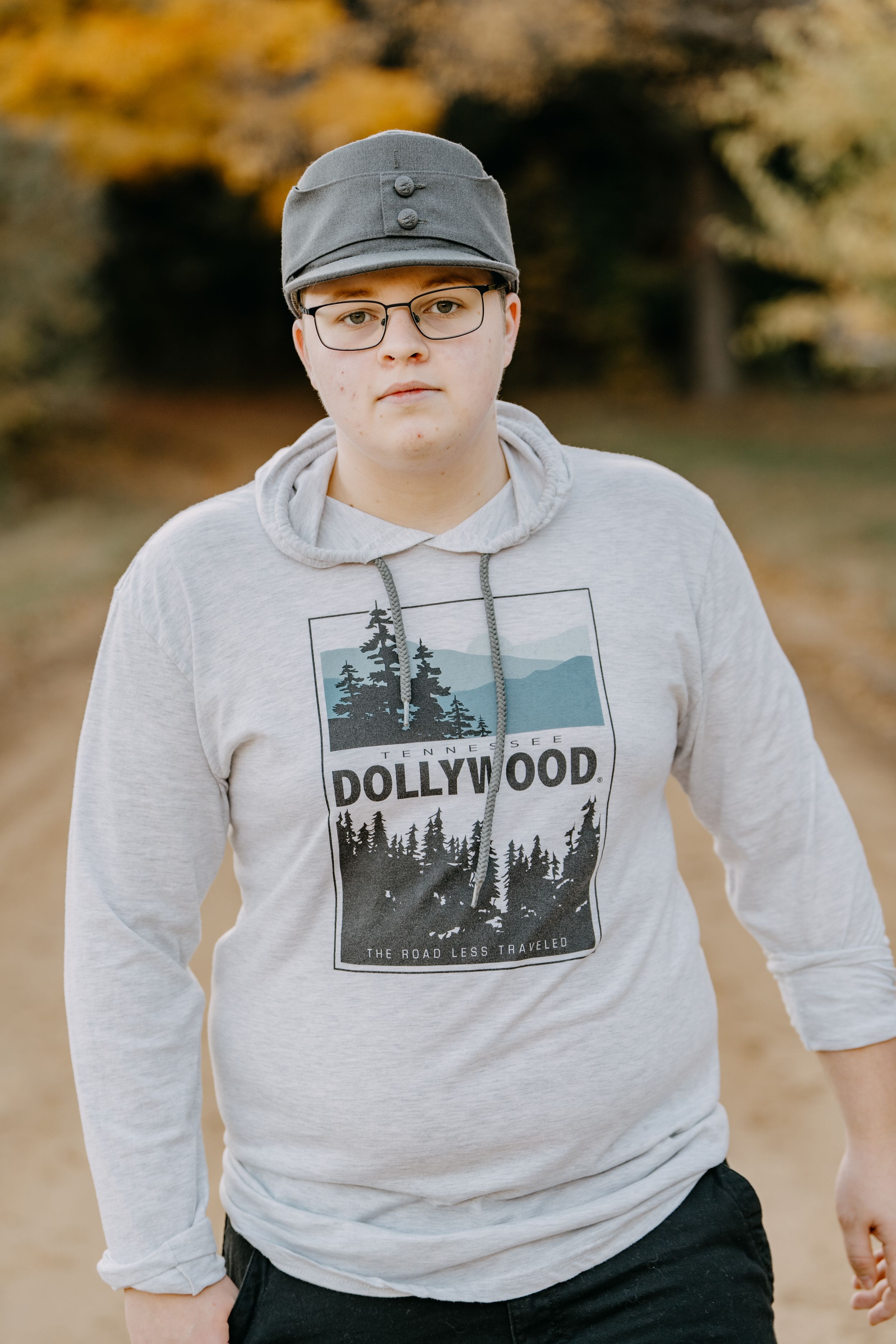 Person in Nike cap and Hollywood graphic sweatshirt poses outdoors during fall season.