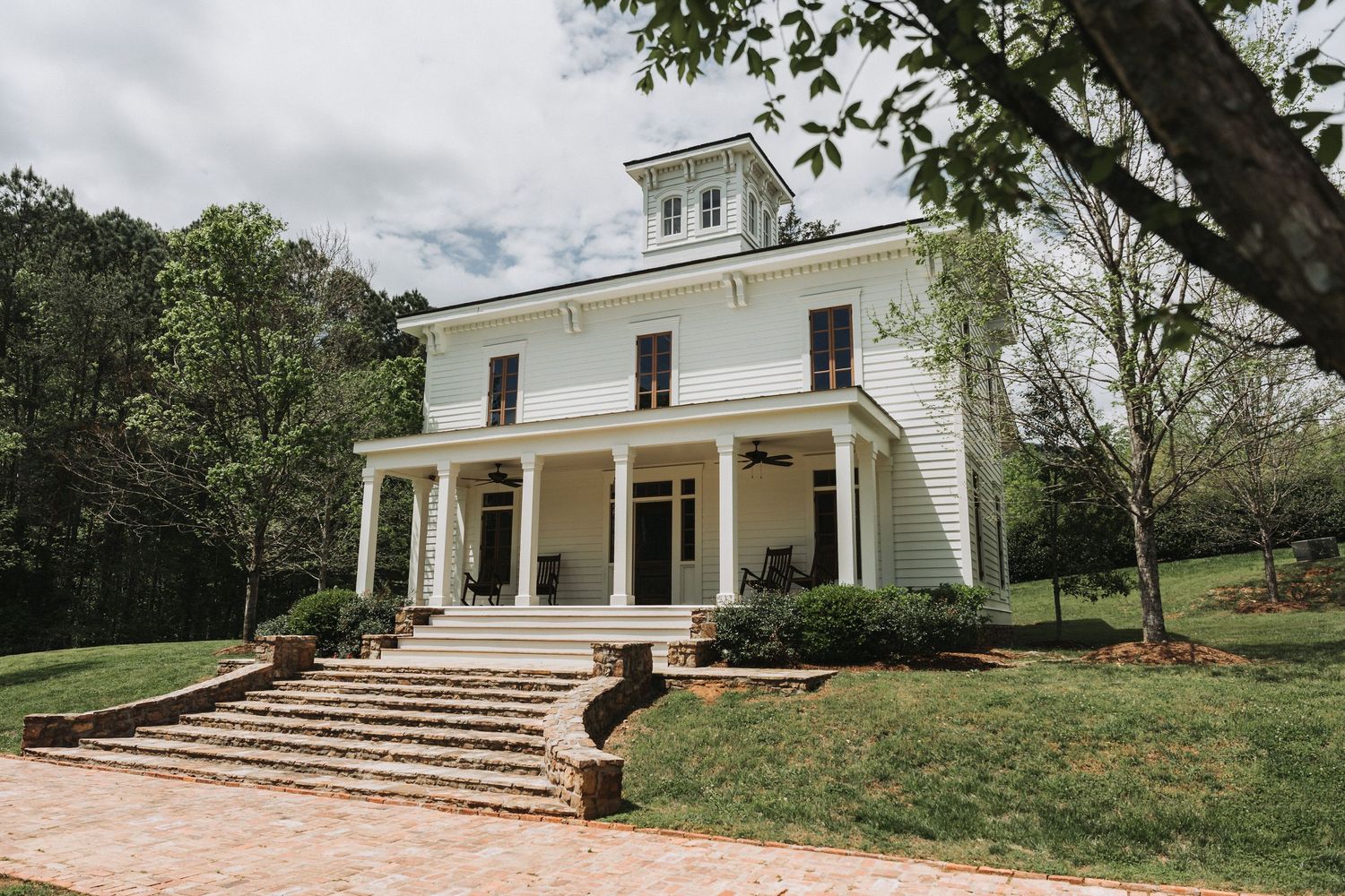 A series of white colonial-style buildings with porches and steps connected by stone walkways in a garden setting.