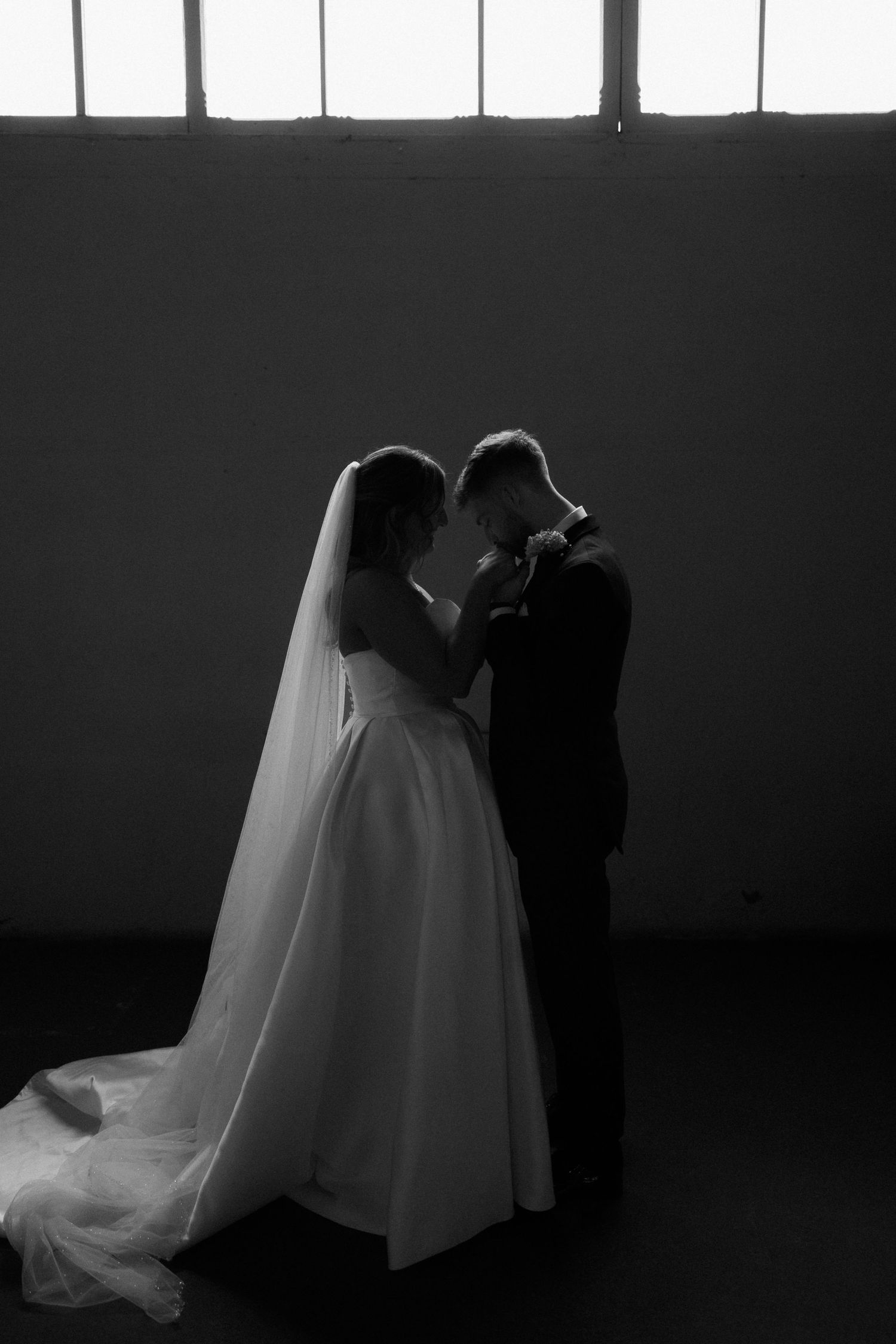 Silhouetted figures in wedding attire against bright windows.