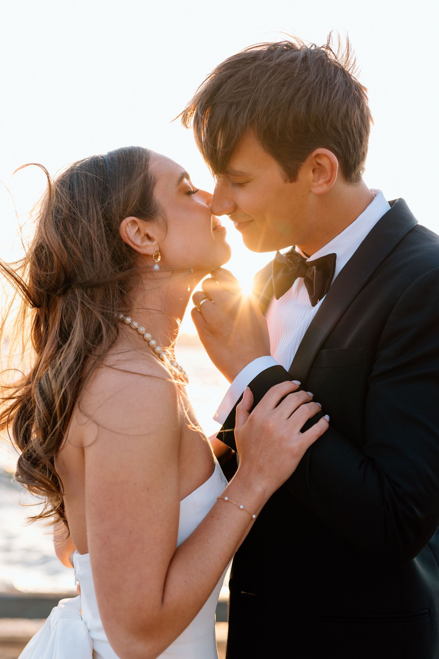 Romantic couple in formal attire share an intimate moment at sunset with golden light glowing behind them.