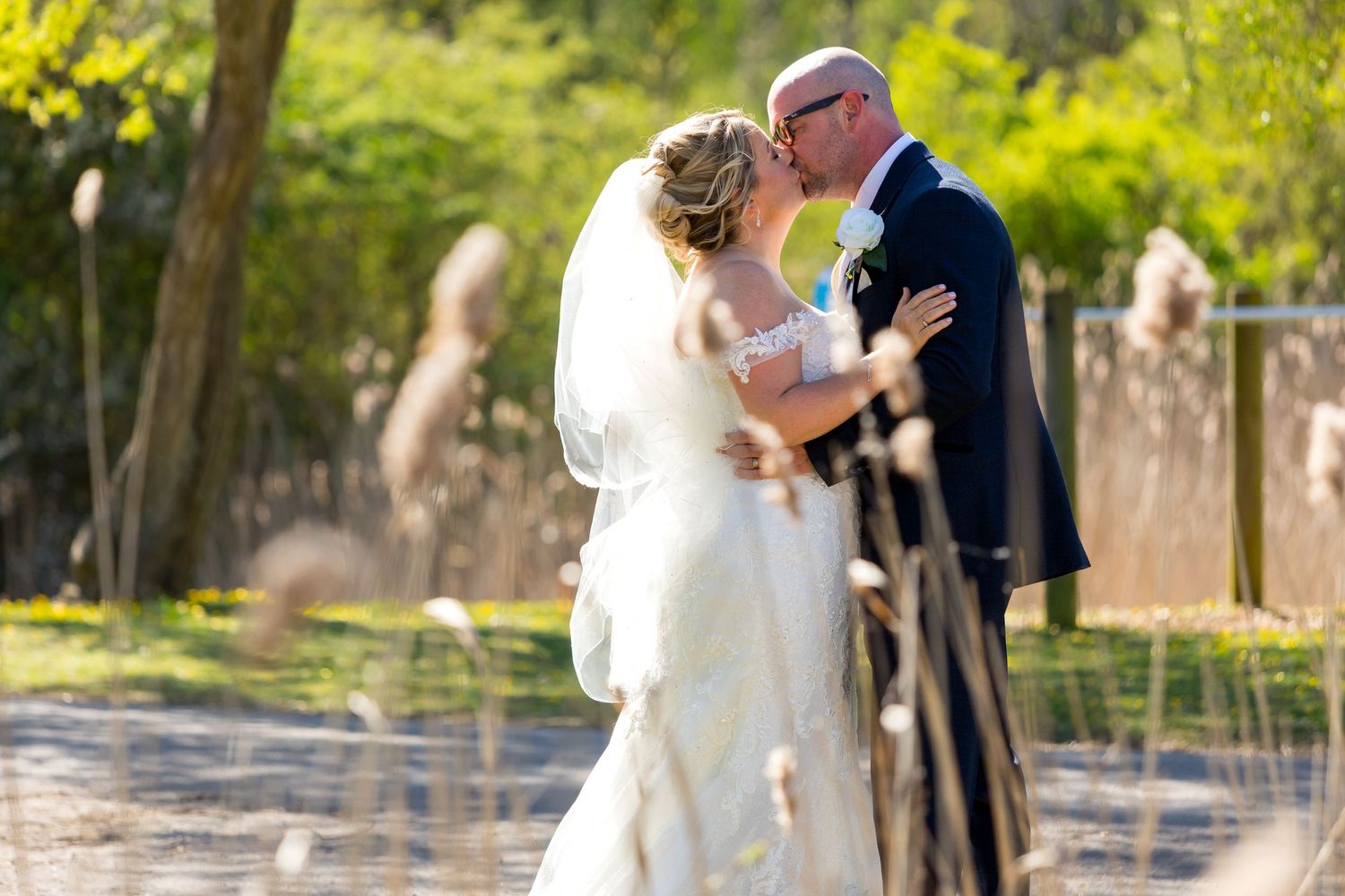 The Village Hotel Wedding Photography share a kiss by the reeds on a sunny spring afternoon.