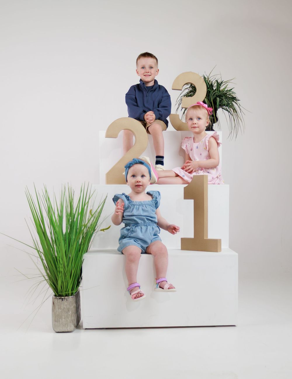 Three children sitting on white steps with decorative numbers and plants.
