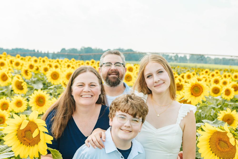 Happy family of four posing together in vibrant sunflower field.