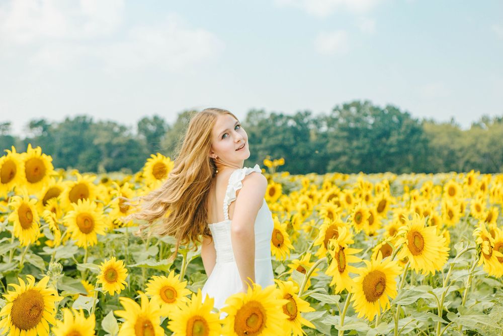 Woman in white dress twirling in blooming sunflower field under blue sky.