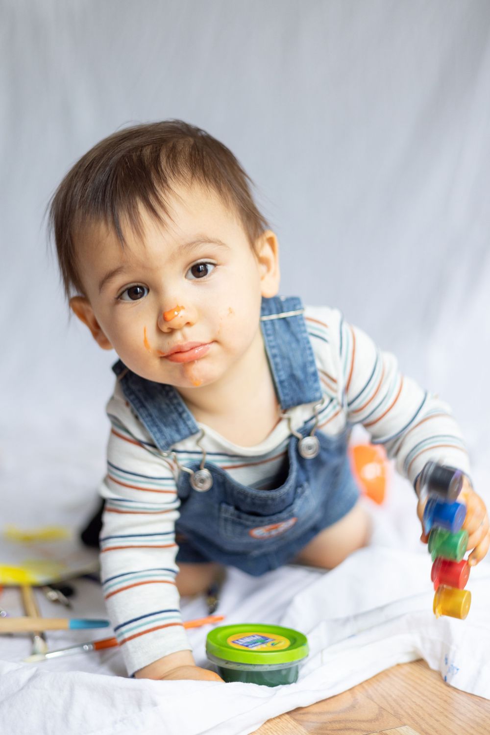 Young toddler in striped shirt and denim overalls playing with colorful toys.