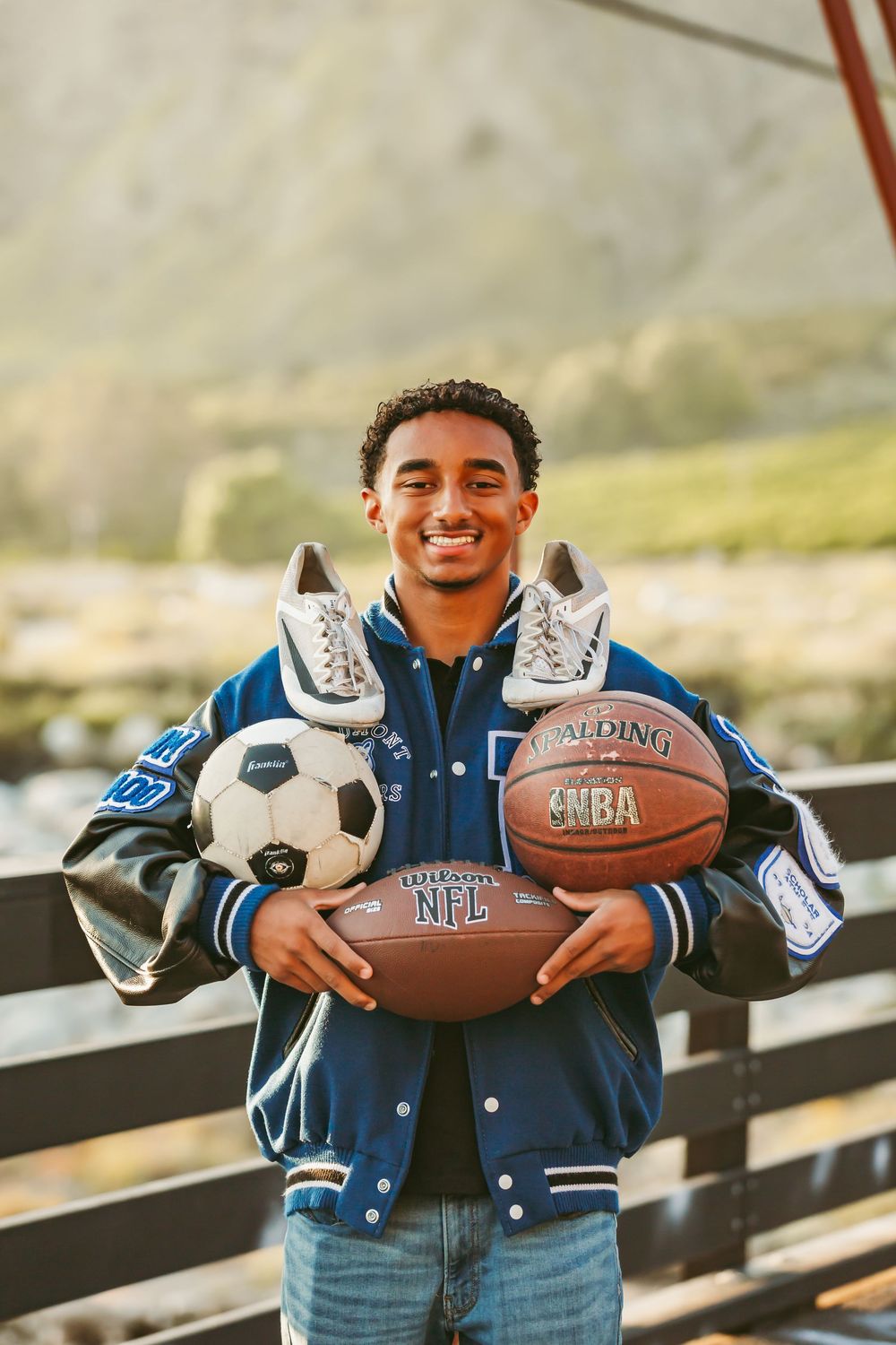 Athletic student poses outdoors with sports equipment including a basketball, soccer ball and sneakers.