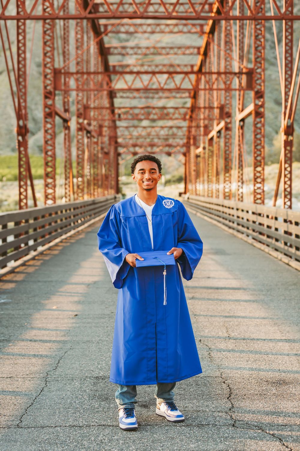 Graduation photos showing someone in a bright blue cap and gown posing on a rustic metal bridge.