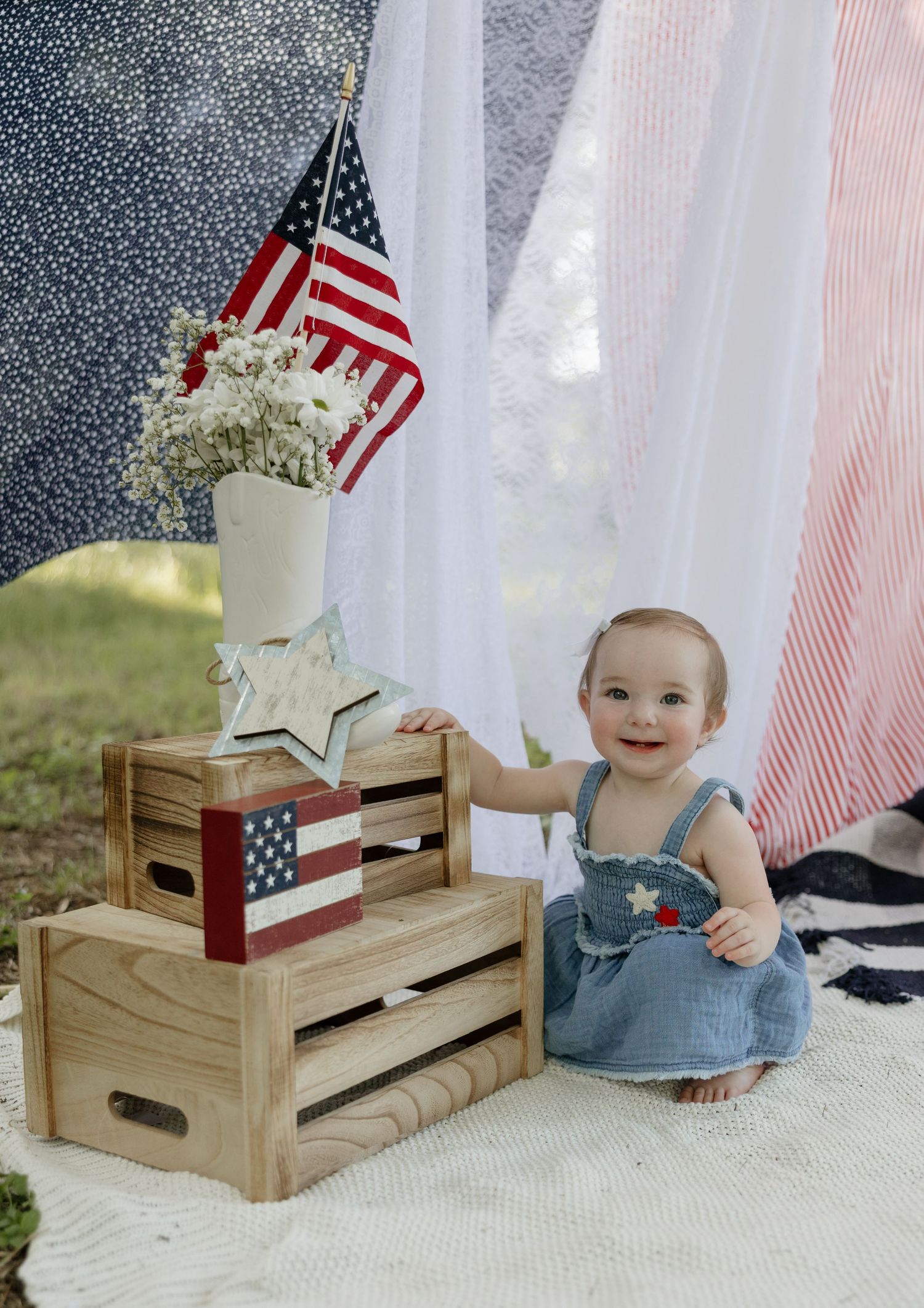 Patriotic holiday setup with wooden crates, American flags and white flowers against a draped backdrop.