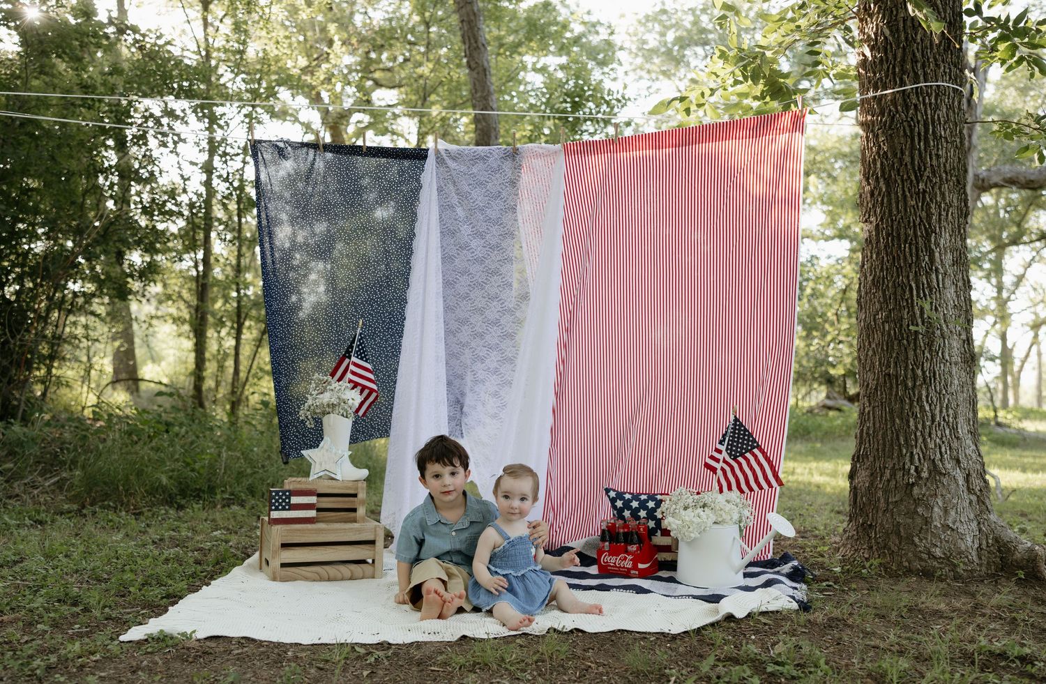 Patriotic outdoor photo setup with American flags, vintage props, and rustic decor against a red white and blue backdrop.