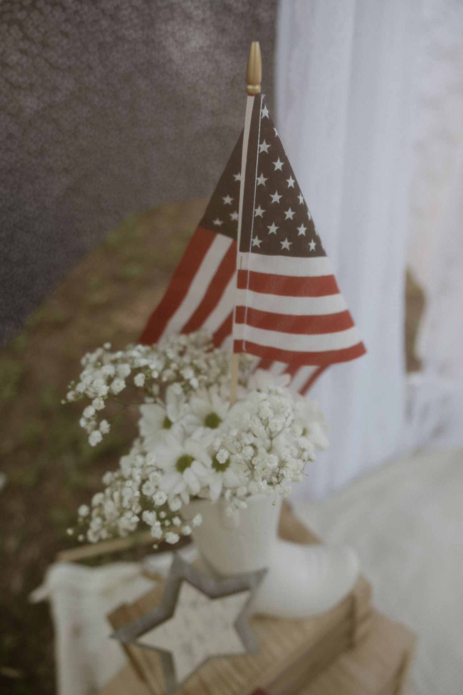 American flags stand alongside delicate white wildflowers in rustic farmhouse decor display against soft background.