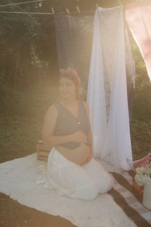 A romantic maternity photo session outdoors with white fabric draping and natural sunlight creating a dreamy atmosphere.