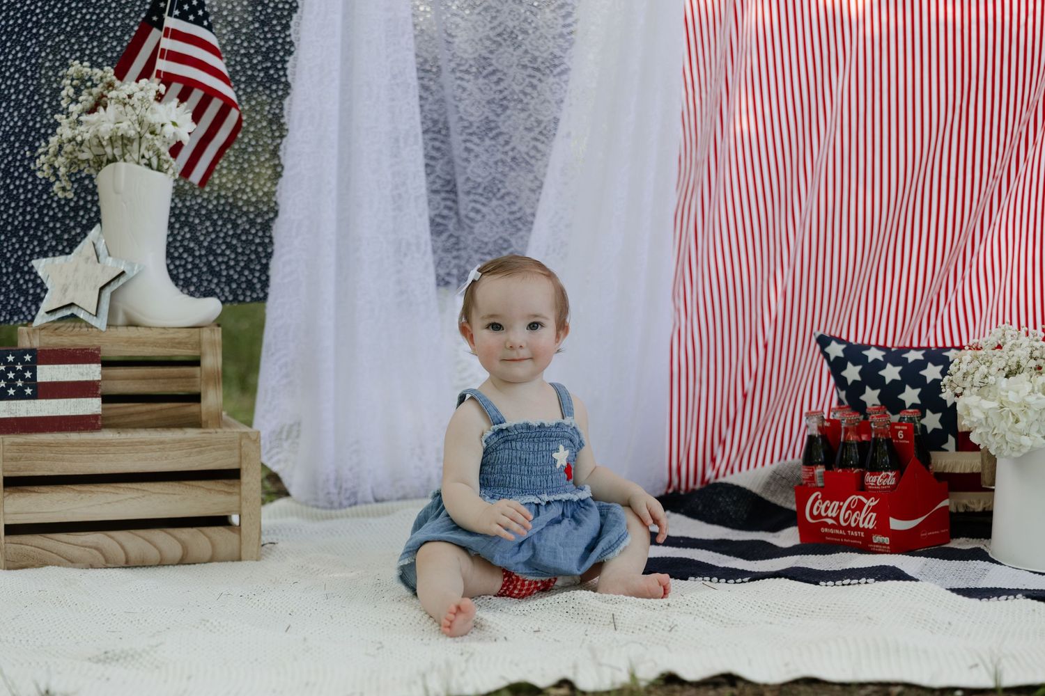 Patriotic themed photo setup with wooden crates, American flag, Coca-Cola crate, and white floral decorations.